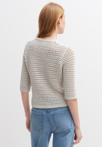 Hellgrauer, gekürzter Pullover mit einem lockeren, offenen Strickdesign. Mit Dreiviertelärmeln und einem runden Ausschnitt, kombiniert mit blauen Jeans.