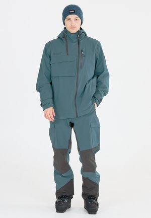 Skijacke und -hose in Teal mit dunkelgrauen Akzenten. Die Jacke hat einen Reißverschluss, mehrere Taschen und einen hohen Kragen. Strukturierte Strickmütze.