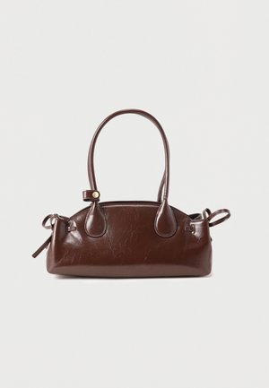 Tmavě hnědá kožená kabelka s dlouhým uchytem, zaoblenými okraji a detaily na bocích s přezkami na jednoduchém světlém pozadí.