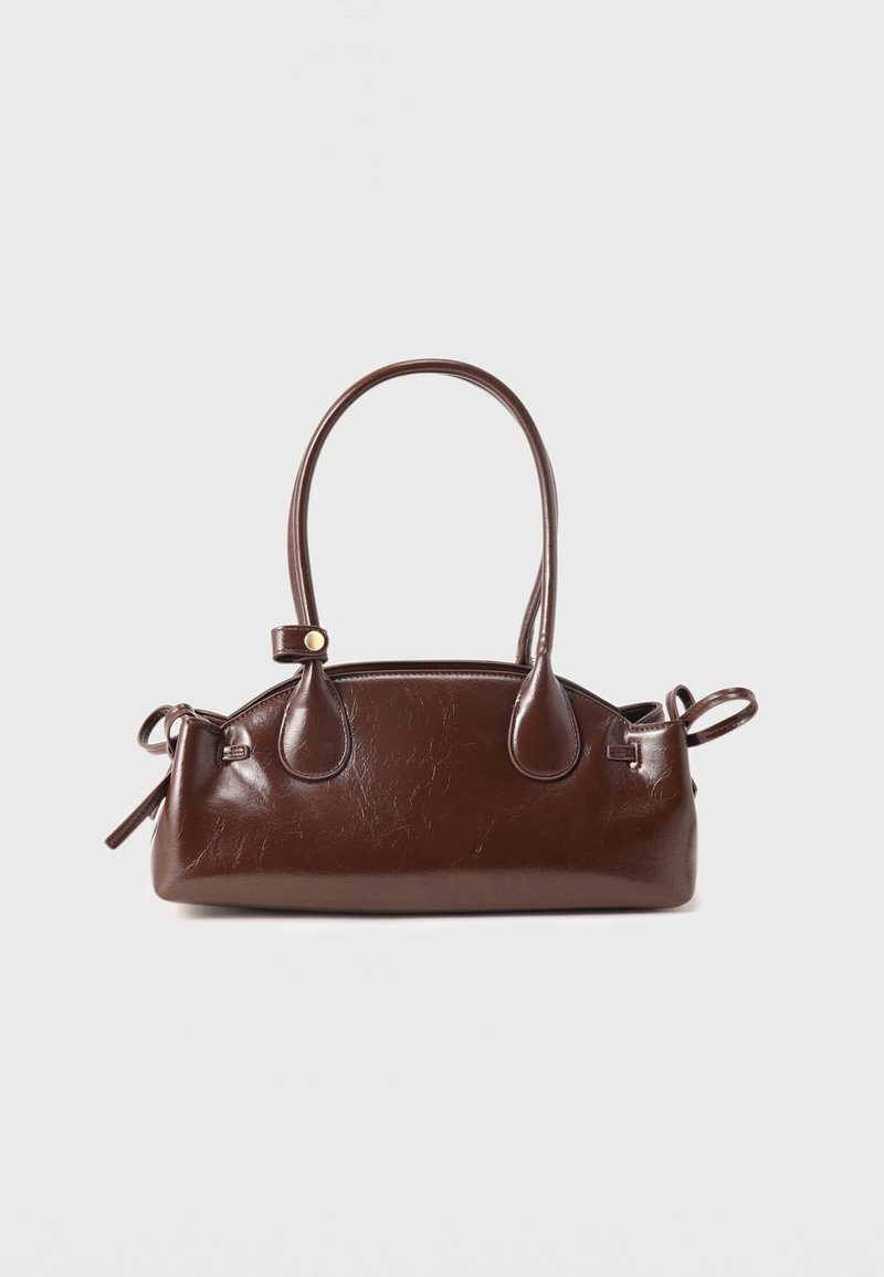 Sac à main en cuir marron foncé avec une longue anse, des bords arrondis et des détails de boucles latérales sur un fond clair uni.