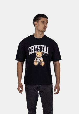 Zwarte katoenen t-shirt met een grafisch ontwerp van een teddybeer en de tekst "CRYSTAL" in het wit, geplaatst tegen een effen achtergrond.
