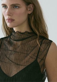 Černý průsvitný top s volánovým vysokým límcem a texturovanou látkou, překrývající pevnou černou vrstvu pod ním. Má měkké švy a elegantní design.