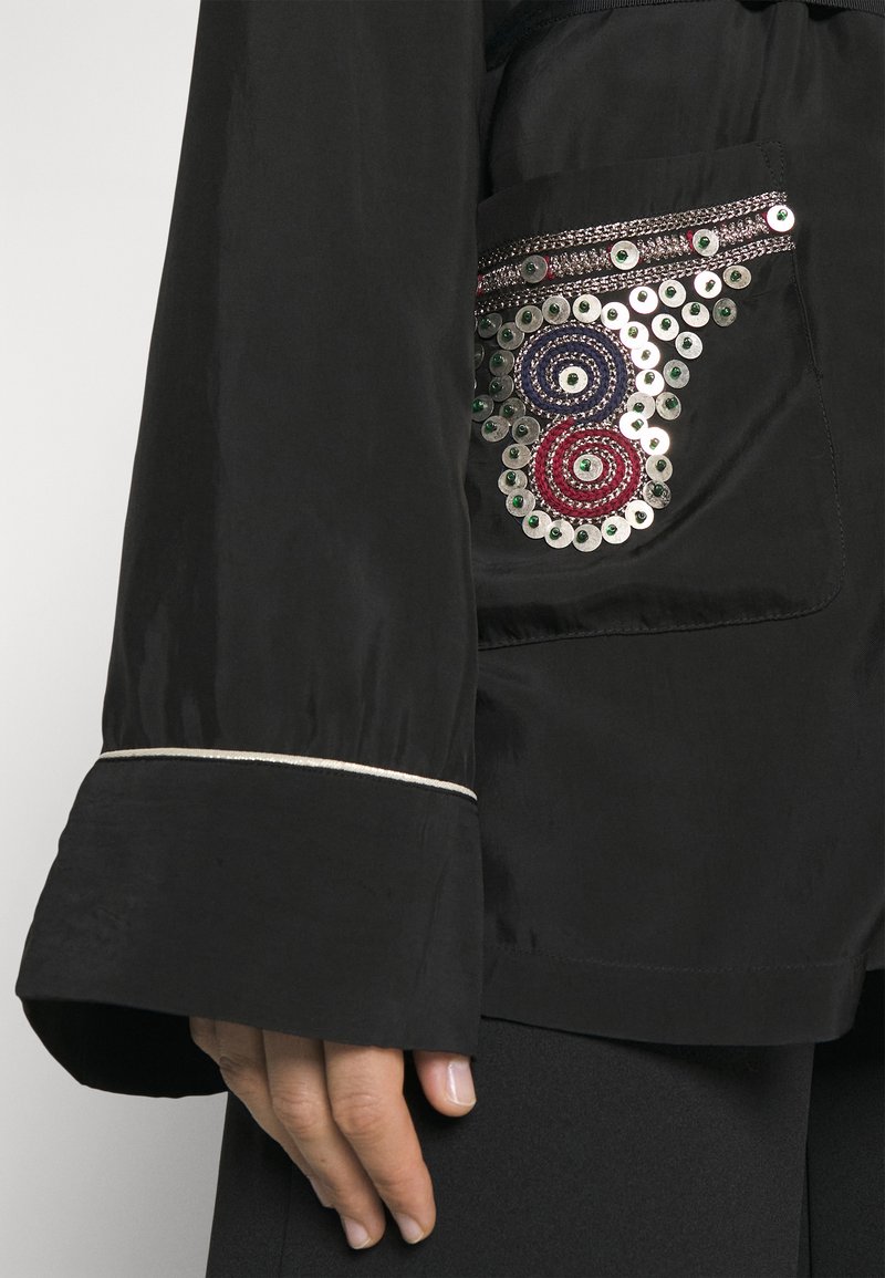 Zwarte jas met een versierde zak met kleurrijke pailletten en ronde borduuraccenten. Lange, losse mouwen met een zilveren trim.