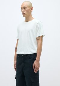 Λευκό βαμβακερό μπλουζάκι με κοντά μανίκια, συνδυασμένο με σκούρο cargo παντελόνι που διαθέτει πολλές τσέπες και κούμπωμα με κουμπί. Μινιμαλιστικός σχεδιασμός.