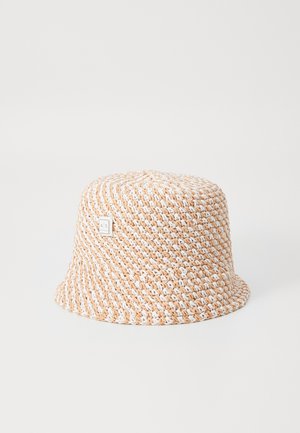 Chapeau bob beige et blanc en crochet avec petite étiquette métallique logo sur fond blanc uni.