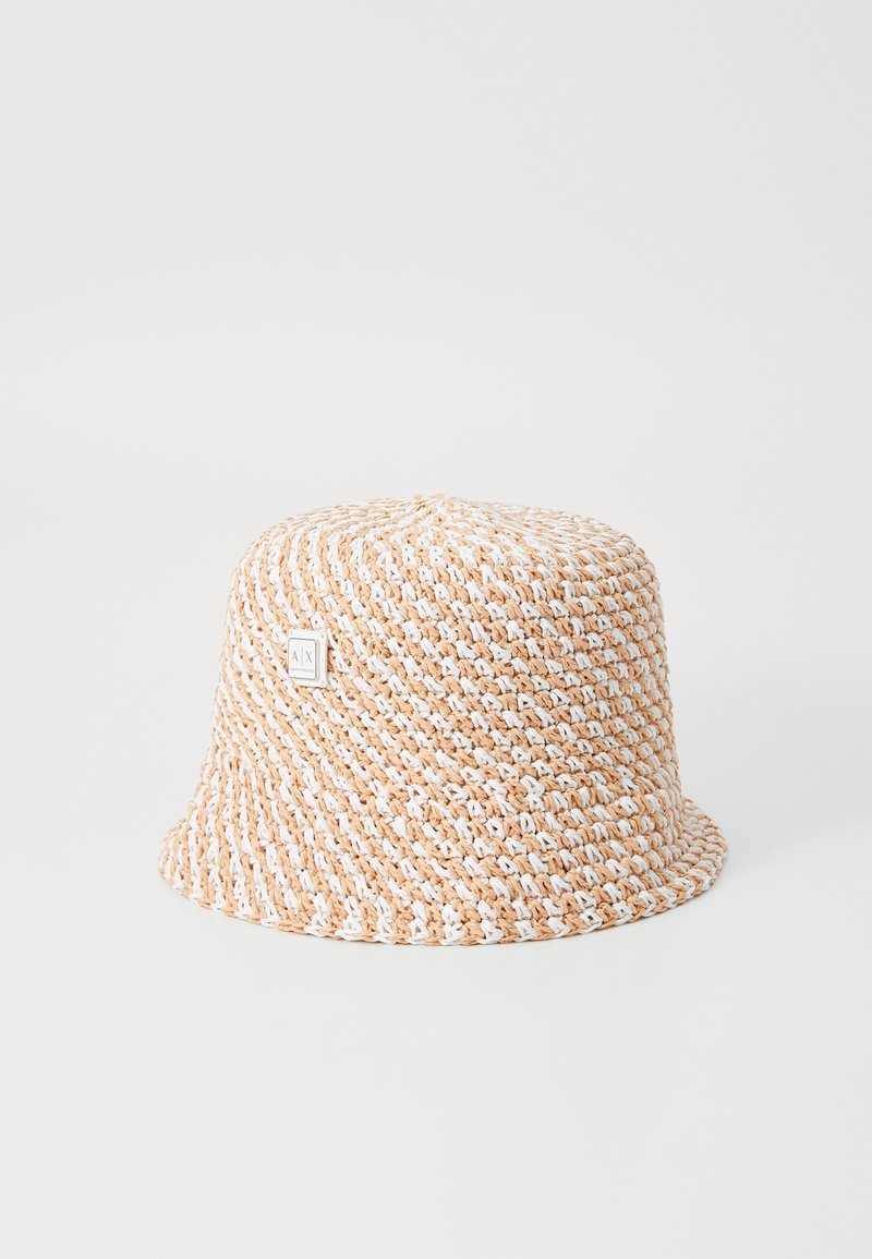 Chapeau bob beige et blanc en crochet avec petite étiquette métallique logo sur fond blanc uni.