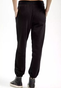 Czarne dresowe spodnie z polaru z elastycznym pasem i ściągaczami, posiadające boczne kieszenie i miękką fakturę, w połączeniu z czarnymi sneakersami typu high-top.