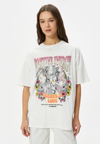 Hvid bomulds T-shirt med en farverig grafisk tryk af skeletter, blomster og tekst. Oversized pasform med korte ærmer og rund halsudskæring.