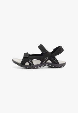 Black open-toe outdoor sandal with adjustable straps, thick sole, and white stitching detail, designed for comfort and durability.