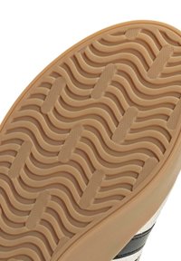 Schoenzool met een getextureerd, golfpatroon in beige rubber. Heeft een gladde bovenzijde en een beige kleur met zwarte accenten.