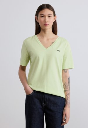 Light green v-neck t-shirt made of soft cotton, featuring short sleeves and a small embroidered logo on the chest. Paired with dark jeans.
