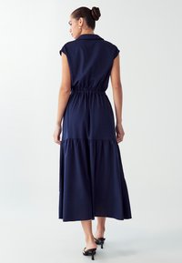 Jūreivių mėlynos spalvos su trumpomis rankovėmis suknelė su elastine juosmens linija ir triukšmingu sijonu. Lygaus audinio, mygtukų užsegimas ant apykaklės ir nugaros detalė.