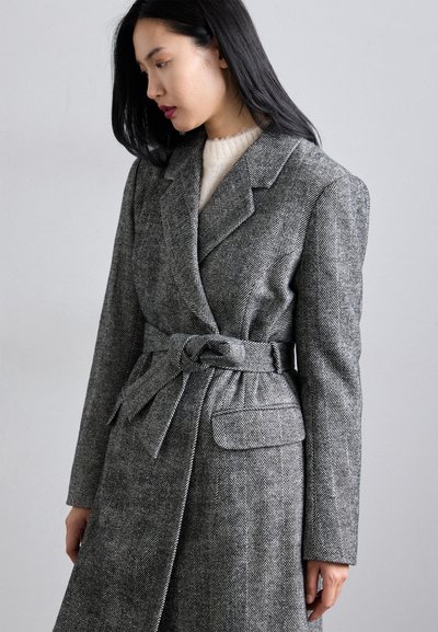 Sivý kabát s károvaným vzorom v štýle houndstooth, ktorý má opasok v páse, klopové vyhrnuté golier a postranné vrecká. Štruktúrovaná tkanina s pevným strihom.