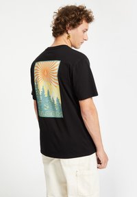 Sort bomulds t-shirt med et farverigt bjerg- og skovgrafik på bagsiden, med orange solstråler og blå accenter. Hvid tekst i bunden.