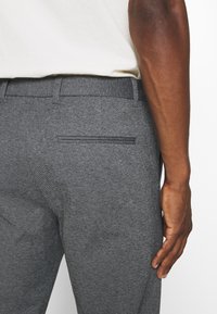 Pantalons gris ajustés en tissu texturé, avec une poche arrière unique, des passants de ceinture et une taille lisse.