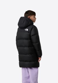 Mustast puffer-stiilis kapuutsiga jakk, millel on tikitud muster, elastsed varrukaservalõiked ja logo seljal. Jakk ulatub kuni reite keskpaigani.