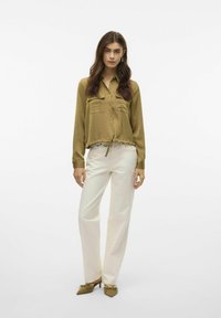 Blusa a maniche lunghe verde oliva con due tasche sul petto, design corto e orlo arricciato, abbinata a pantaloni bianchi a gamba dritta e tacchi verde.