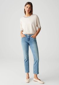 Helles beiges, verkürztes Sweatshirt mit schwarzem Saum, kombiniert mit hellblauen, geraden Jeans. Die Schuhe sind cremefarbene, slip-on Ballerinas. Einfacher, lässiger Look.