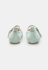 Zelene suede čevlje z zaobljenim nosom, ravnim podplatom in zadnjim trakom z nastavljivo zaponko. Teksturna površina z brezšivnim dizajnom.