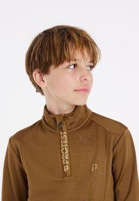 Bruine ritstrui met hoge kraag, voorzien van een logo op de borst en een contrasterende rits. Gladde, rekbare stof.