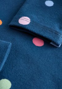 Mørkeblå stof med farverige polkaprikker i pink, orange, lyseblå og grøn. Blød tekstur med en foldet manchet synlig. Søm detalje.