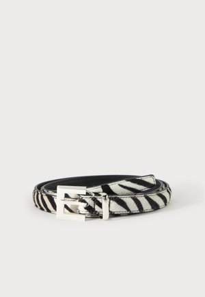 Ceinture zébrée noire et blanche avec une boucle rectangulaire argentée, enroulée sur un fond clair uni.
