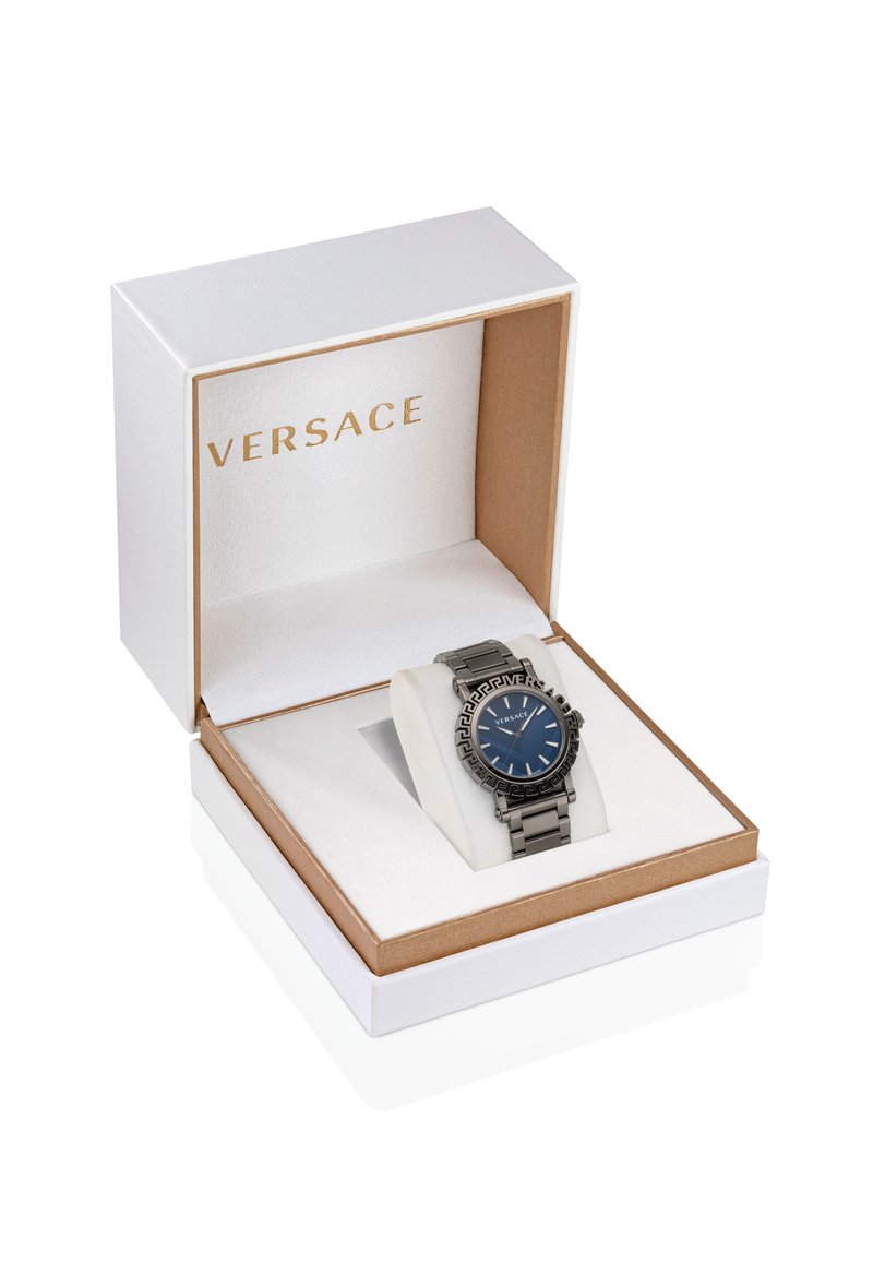 Versace-Uhr in einer weißen und goldenen Box. Sie verfügt über ein blaues Zifferblatt, ein silberfarbenes Metallarmband und ein rundes Gehäuse mit kunstvollen Lünette-Details.