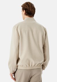 Sudadera beige con cuello alto, puños elásticos y dobladillo inferior. Textura suave, diseño casual y estilo minimalista.