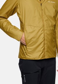 Yellow insulated jacket with a front zipper, side pockets, and a smooth texture, paired with black pants featuring a zippered pocket.