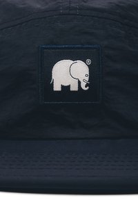 Námořnická modrá čepice s obdélníkovou vyšívanou nášivkou s bílým designem slona a logem. Materiál je texturovaný, s perforovaným okrajem.