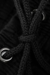 Cordon de zapato negro de nailon tejido con una trenza texturizada, pasado a través de un ojal de metal plateado, asegurado con un nudo.