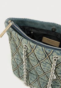 Borsa tote in denim con motivo trapuntato, manici a catena argentata e chiusura con zip. Interno foderato in nero con una tasca. Etichette visibili.