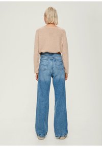 Maglietta a maniche lunghe a righe marrone chiaro abbinata a jeans a vita alta blu chiaro a gamba larga, con due tasche posteriori e dettagli sfrangiati.