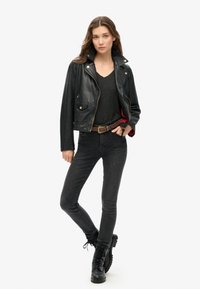 Sort læder bikerjakke med guld hardware, båret over en mørkegrå V-hals top. Sættes sammen med sorte skinny jeans og snørebånds sorte støvler.