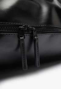 Bolsa negra con cremallera que presenta dos tiradores metálicos, material texturizado y un diseño elegante con costuras visibles a lo largo de los bordes.