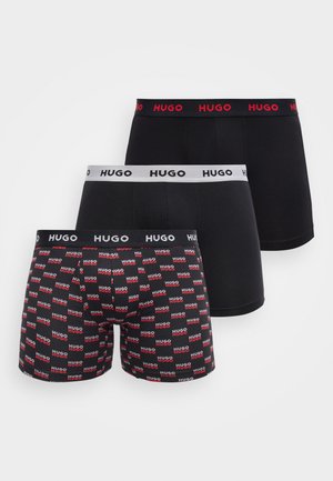 Tri páry čiernych boxeriek, každá s iným pásom s nápisom „HUGO“ a jedna para pokrytá červenými a bielymi logami „HUGO“.