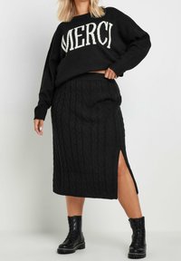 Mustasynttapaita, jossa on valkoisella "MERCI"-teksti, yhdistetty musta nyörineulehame, jossa on sivuaukot. Raskaat mustat maihinnousukengät viimeistelevät asukokonaisuuden.