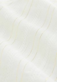 Tissu blanc avec des rayures dorées, présentant un motif texturé de lignes ondulées et de délicates accents en dentelle. Matériau doux et léger.