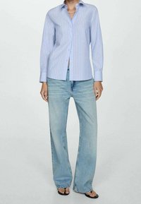 Chemise à manches longues rayée bleu clair avec un col, une patte de boutonnage à l'avant et des poignets ajustés, associée à un jean bleu clair à jambes larges.