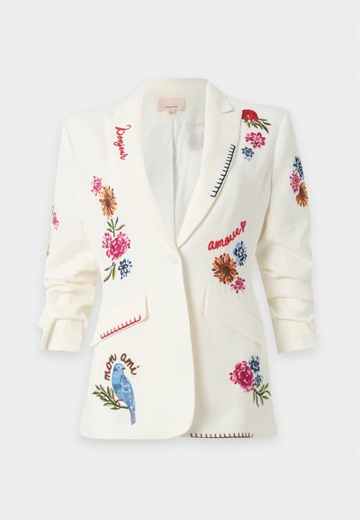 Blazer blanc avec broderies florales colorées, oiseau bleu et mots français comme "bonjour", "amour" et "mon ami" sur le devant et les manches.