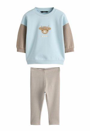 Maglietta a maniche lunghe azzurro chiaro per bambino con maniche beige e volto di mucca lavorato a maglia, abbinata a leggings beige e bianchi a righe.