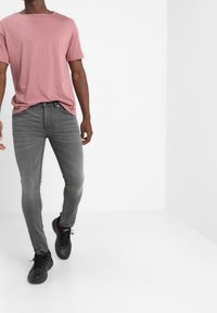 Ljusrosa t-shirt med kort ärm i kombination med tajta grå jeans. Jeansen har en lätt nötta textur och en smal silhuett. Svarta sportskor fulländar outfiten.