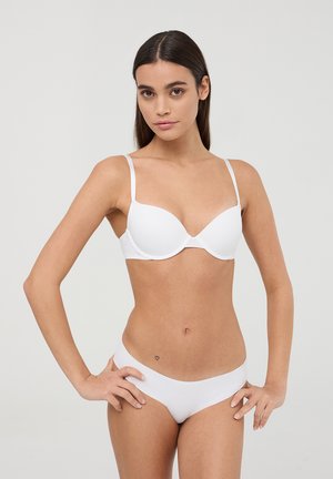 Reggiseno bianco imbottito con spalline sottili, design senza cuciture e texture liscia. La biancheria intima bianca coordinata presenta un taglio a vita bassa e dettagli minimi.