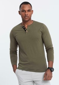 Maglietta henley a maniche lunghe verde oliva con una patta a bottoni nera, caratterizzata da bottoni in legno e un tessuto morbido e testurizzato.