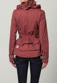 Roodbruin jack met een gerimpelde capuchon en een gelaagd ontwerp aan de achterkant. Voorzien van knoopmanchetten en een taillekoord. Geweven label zichtbaar aan de onderkant.