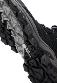 Black hiking shoe with a textured, patterned rubber sole featuring deep lugs for traction. Includes light gray accents and branding detail.