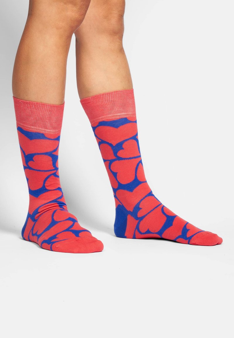Kleurige kniehoge sokken met een rood hartpatroon op een blauwe achtergrond, voorzien van een roze geribbelde boord en een gladde textuur.