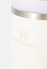 Gobelet en acier inoxydable isolé avec une finition blanc mat, doté d'un bandeau argenté et d'un logo en relief subtil d'un lion avec des ailes.