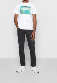 Camiseta de algodón blanca con un gráfico colorido de Levi's en el frente, combinada con pantalones gris oscuro y zapatillas blancas con suelas negras.