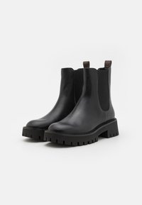 Black leather Chelsea ankle boots with elastic side panels, textured rubber soles, and pull tabs for easy wearing.